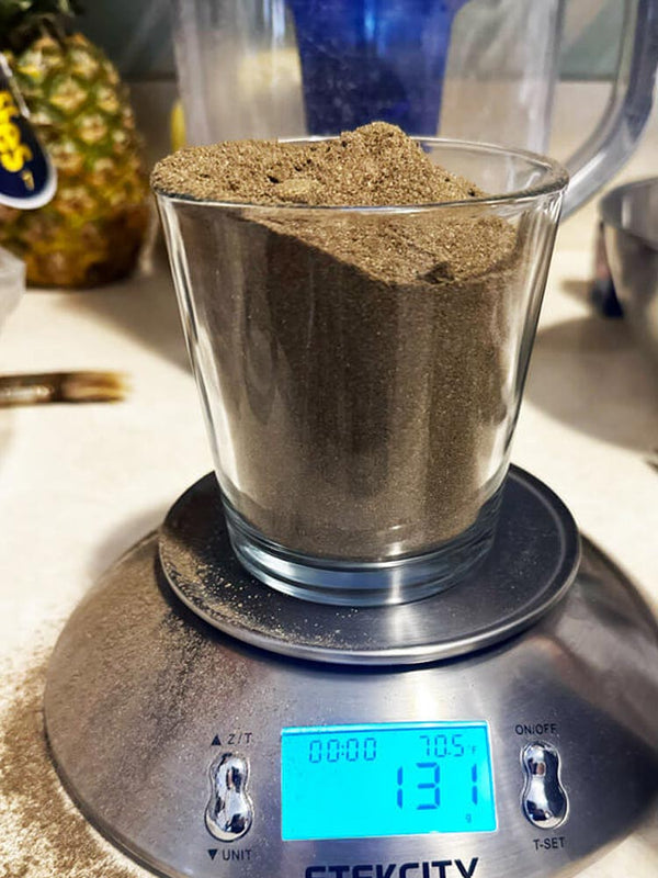 Glass container with brown powder on a digital scale, with a pineapple in the background.